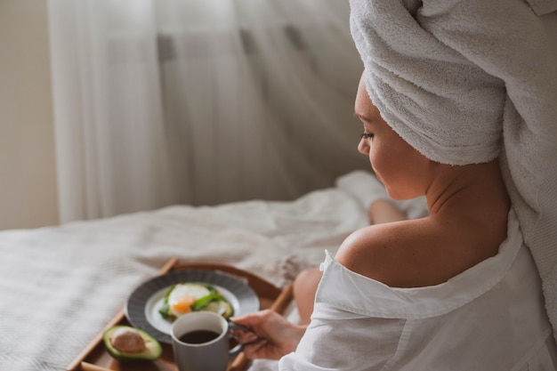 Hermosa chica con una toalla blanca en la cabeza se sienta en la cama por la mañana y bebe café