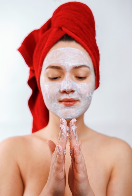 Hermosa chica con una toalla roja en la cabeza aplica un exfoliante en la cara