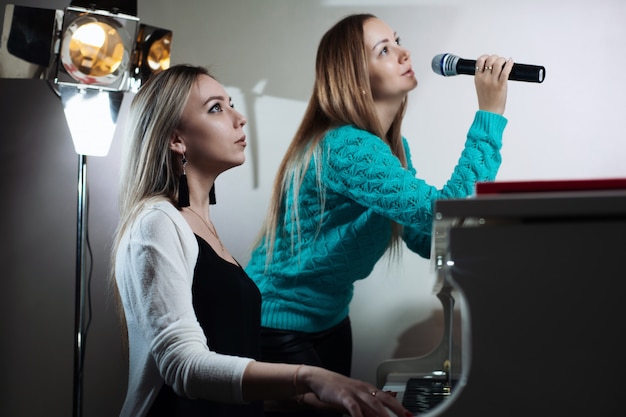 Foto hermosa chica tocando el piano y su amiga canta en el micrófono