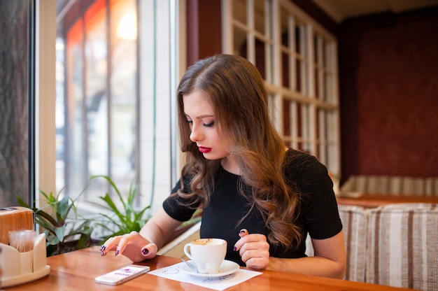 Hermosa chica tomando café y mirando en el teléfono