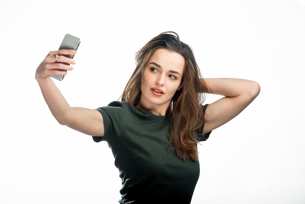 Hermosa chica tomando selfie sobre fondo blanco de estudio Mujer joven de pelo largo toma una selfie en su teléfono inteligente