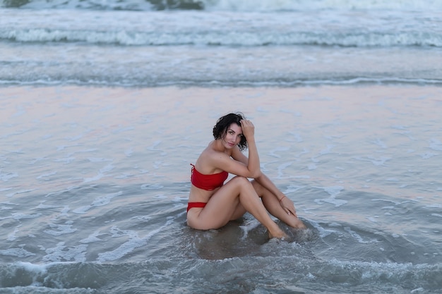 Hermosa chica en traje de baño rojo toma el sol en un muelle de hormigón con el fondo del mar azul