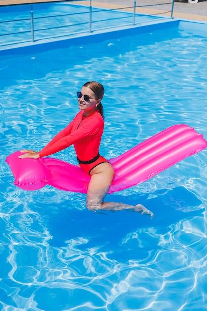 Hermosa chica en traje de baño rosa relajándose en un colchón rosa inflable en la piscina Una mujer delgada y caliente con gafas de sol y trajes de baño está tomando el sol Una mujer se está relajando en un resort de lujo