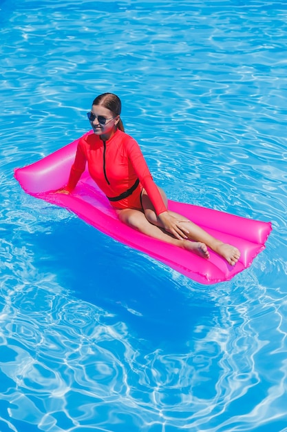 Hermosa chica en traje de baño rosa relajándose en un colchón rosa inflable en la piscina Una mujer delgada y caliente con gafas de sol y trajes de baño está tomando el sol Una mujer se está relajando en un resort de lujo