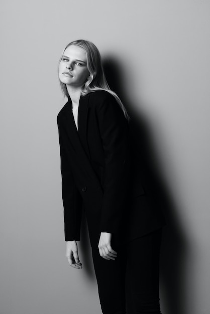 Una hermosa chica con un traje clásico mira a la cámara y se inclina hacia adelante posando en el estudio Fotografía en blanco y negro Fotografía estilística