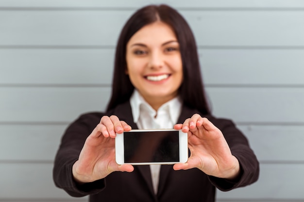 Hermosa chica en traje clásico mostrando teléfono móvil.