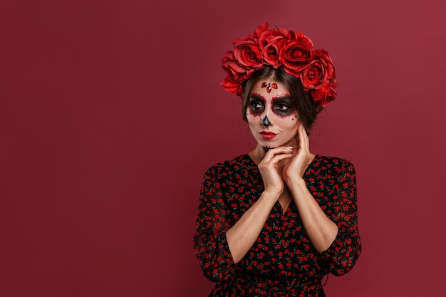 Hermosa chica en traje de la muerta y maquillaje de calavera mirando a la cámara durante halloween