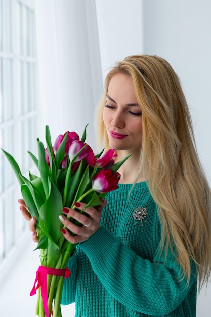 Hermosa chica con tulipanes junto a la ventana