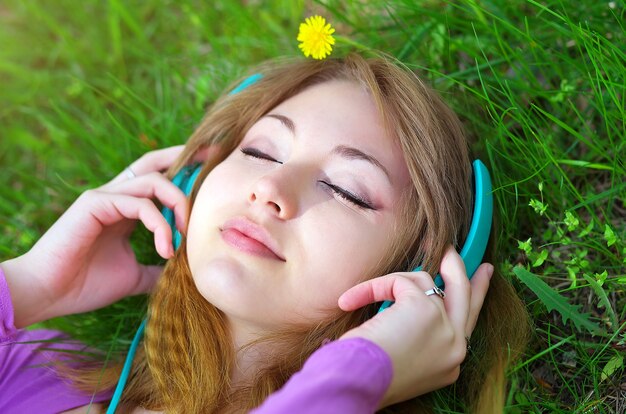 Hermosa chica tumbada en el césped y escuchando música con auriculares en el parque