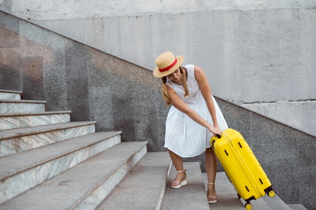 Hermosa chica turista viaja. Sube una gran maleta amarilla por los escalones. Carga pesada. Copie el espacio.