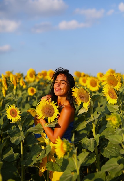 Foto hermosa chica ucraniana, parada en un campo de girasoles, envuelta en una bandera nacional