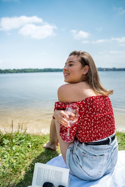 Hermosa chica usa ropa informal, sostenga una copa de champán o vino blanco, solo descanse cerca del lago el día de verano