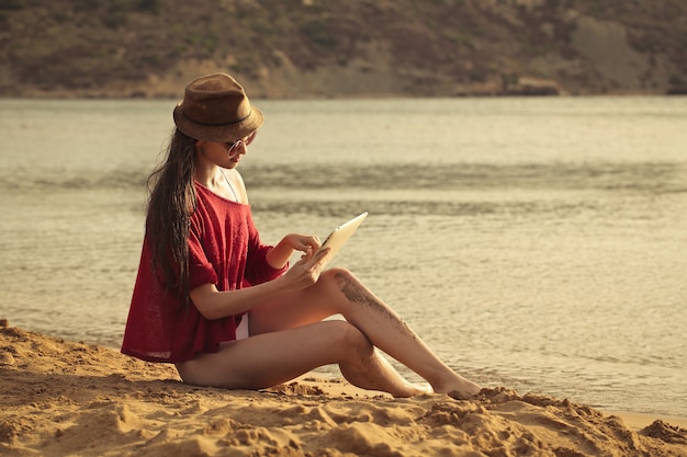 Hermosa chica usando una tableta en la playa