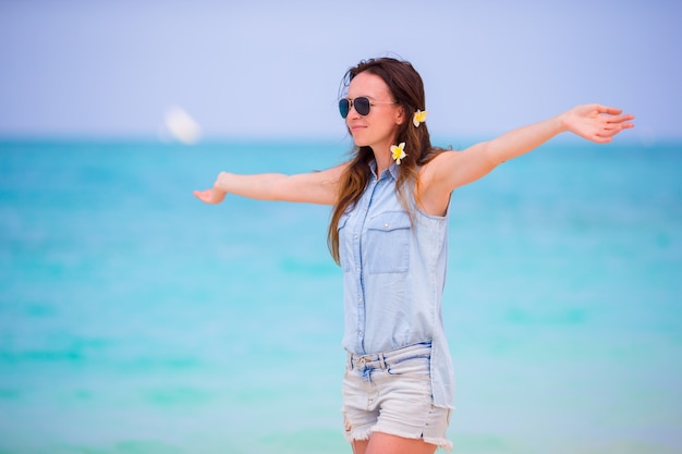 Hermosa chica durante las vacaciones de playa tropical. Disfruta de unas vacaciones de verano solo en la playa de África con flores de frangipani en el pelo