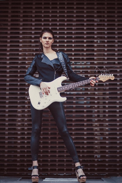 Hermosa chica vestida de negro posa con guitarra eléctrica