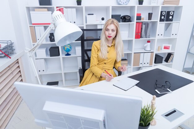 Hermosa chica en vestido amarillo escribe en su diario en su lugar de trabajo