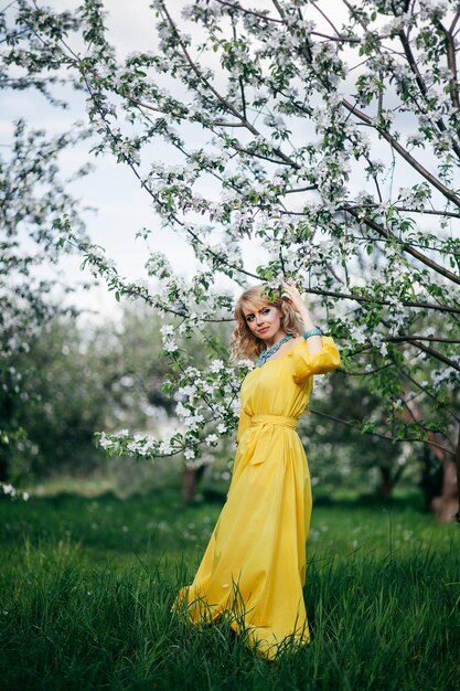 Hermosa chica con vestido amarillo en un jardín floreciente