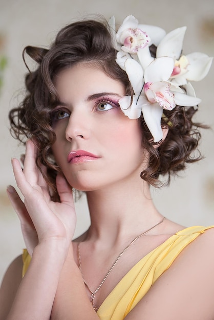 Hermosa chica con un vestido amarillo con orquídeas en el pelo