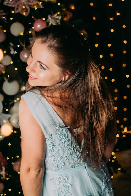 Hermosa chica con un vestido azul con el telón de fondo de un árbol de Navidad y luces de año nuevo