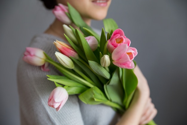 Hermosa chica en el vestido azul con tulipanes flores en manos sobre un fondo claro