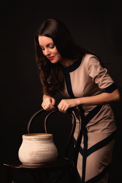 Hermosa chica con un vestido beige y una jarra sobre un fondo oscuro