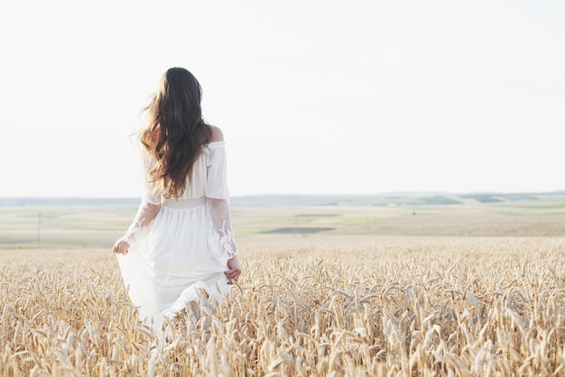 Hermosa chica en vestido blanco corriendo en el campo de trigo de otoño al atardecer