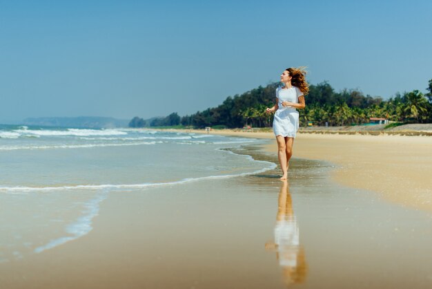 Hermosa chica en vestido blanco corriendo en la playa