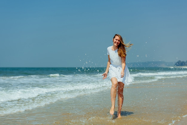 Hermosa chica en vestido blanco disfruta y relájate en la playa