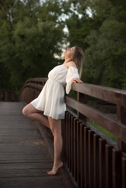 Una hermosa chica con un vestido blanco se encuentra en un puente de madera.