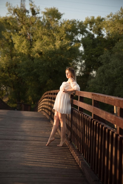 Una hermosa chica con un vestido blanco se encuentra en un puente de madera.