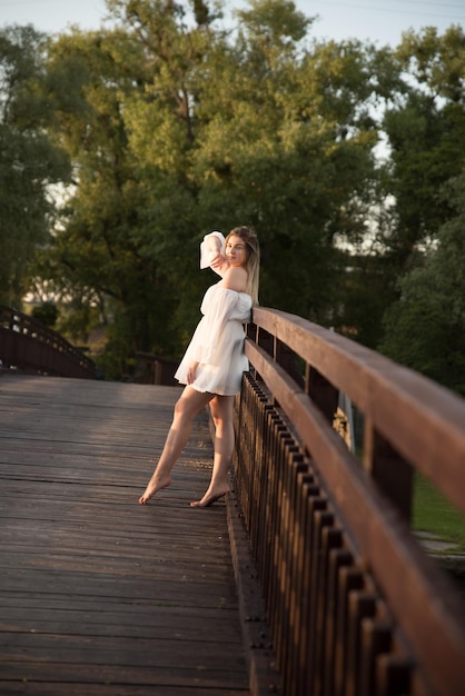 Una hermosa chica con un vestido blanco se encuentra en un puente de madera.