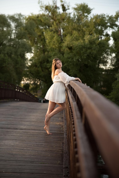 Una hermosa chica con un vestido blanco se encuentra en un puente de madera.