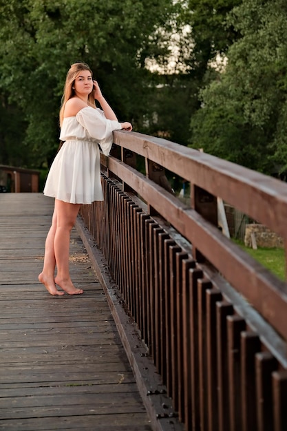 Una hermosa chica con un vestido blanco se encuentra en un puente de madera.