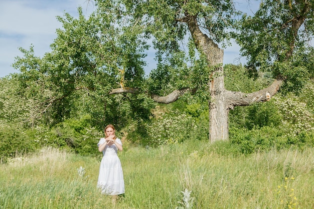 Hermosa chica con un vestido blanco con flores en un campo con vista al cielo