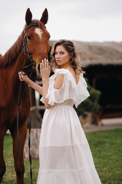 Hermosa chica con un vestido blanco junto a un caballo en un antiguo rancho