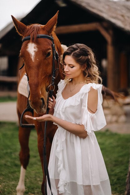 Hermosa chica con un vestido blanco junto a un caballo en un antiguo rancho