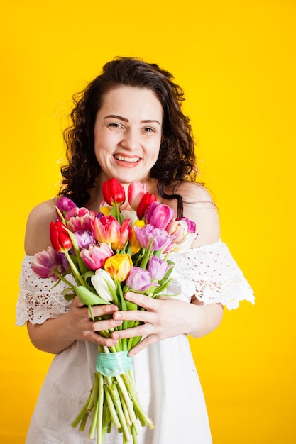 Hermosa chica en el vestido blanco con tulipanes de flores en las manos