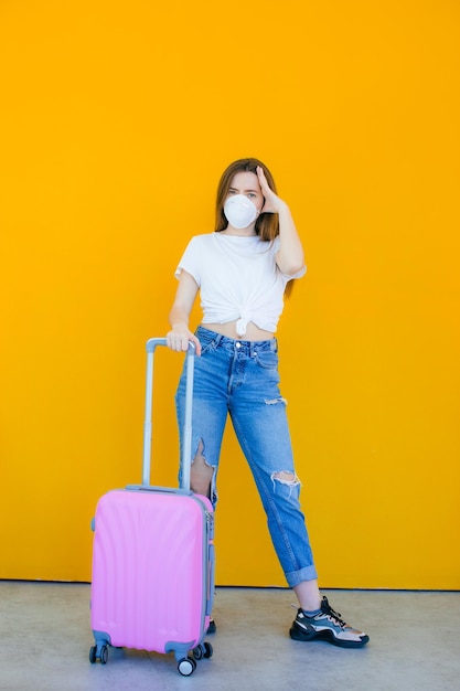 Hermosa chica con un vestido blanco de verano con una maleta Máscara médica en la cara