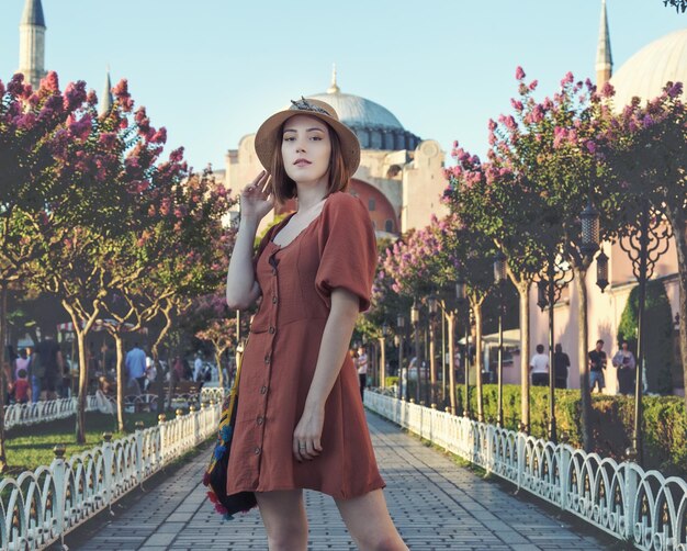 Hermosa chica con vestido de color naranja posando con Hagia Sophia durante la puesta de sol desde Estambul