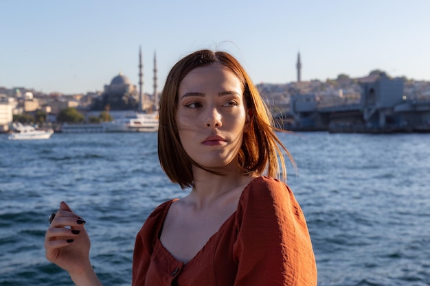 Hermosa chica con vestido de color naranja posando con el puente Galata y las mezquitas de Estambul