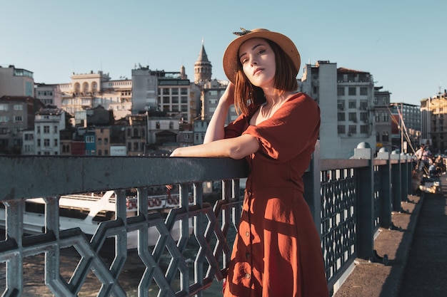 Hermosa chica con vestido de color naranja posando en el puente de Galata con la torre de Galata