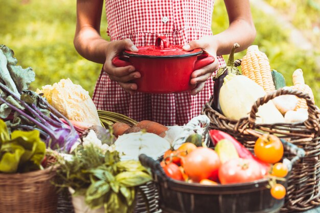 Hermosa chica con un vestido a cuadros juega con una variedad de verduras en el césped