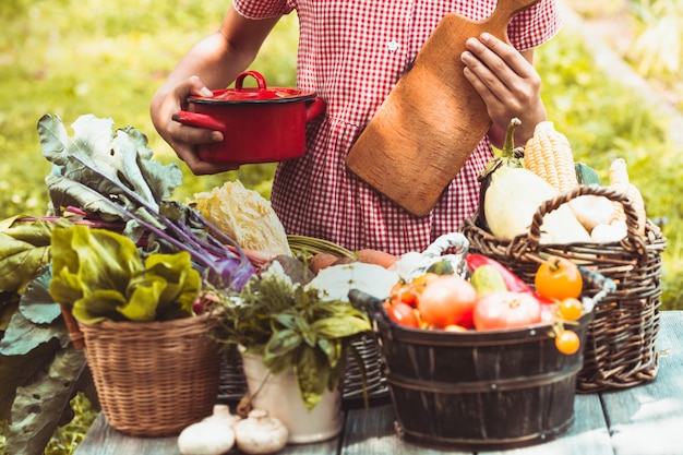 Hermosa chica con un vestido a cuadros juega con una variedad de verduras en el césped