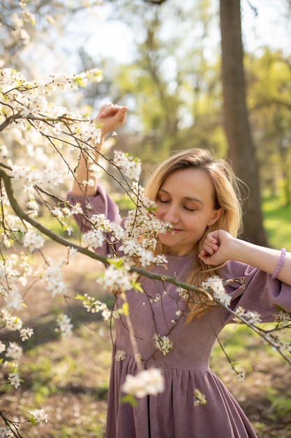 Hermosa chica con un vestido disfruta del aroma de un árbol en flor Parque de primavera Concepto del día internacional de la mujer