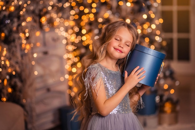 Hermosa chica con un vestido elegante con el telón de fondo de las luces de Navidad y un árbol de Navidad en un hermoso interior