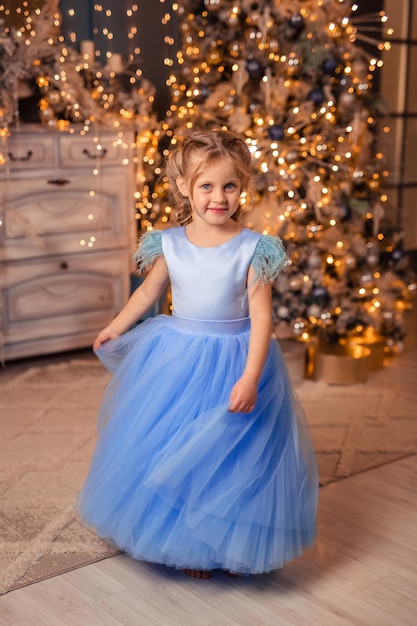 Hermosa chica con un vestido elegante con el telón de fondo de las luces de Navidad y un árbol de Navidad en un hermoso interior