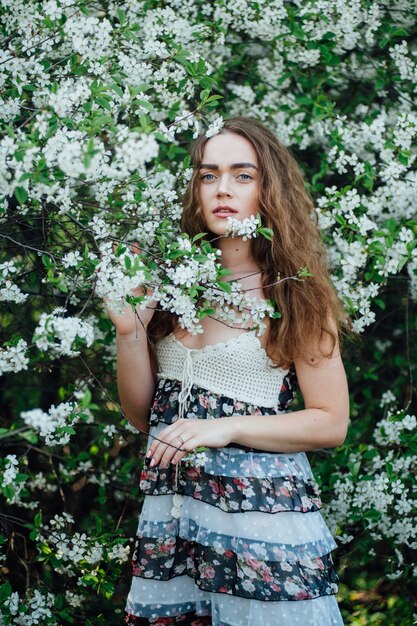 Una hermosa chica con un vestido se encuentra junto a un autobús de cerezas en flor