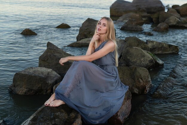 hermosa chica con un vestido gris junto al mar al atardecer