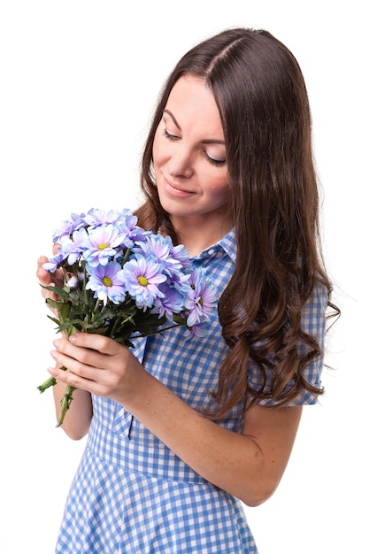 Hermosa chica con un vestido en una jaula azul con crisantemos de flores en las manos sobre un fondo blanco