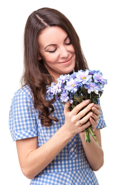 Hermosa chica con un vestido en una jaula azul con crisantemos de flores en las manos sobre un fondo blanco